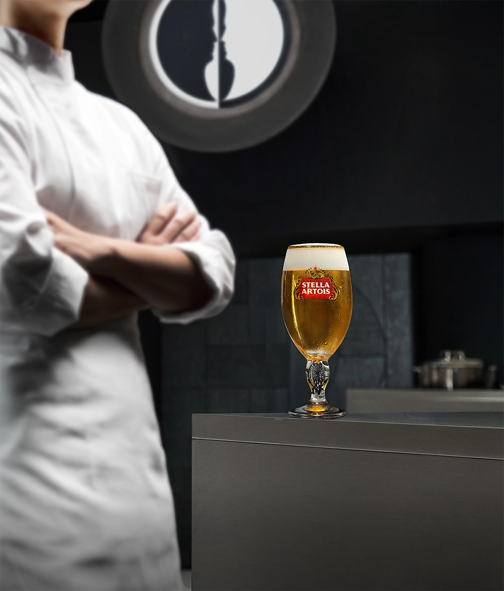 스텔라 아르투아와 콜라보한 넷플릭스 흑백요리사 시즌2 무대 배경으로 흑 요리사와 백 쉐프 경쟁 구조로 등을 지닌채 있으며, 배경으로 흑백요리사 로고와 챌리스잔에 생맥주가 보입니다.